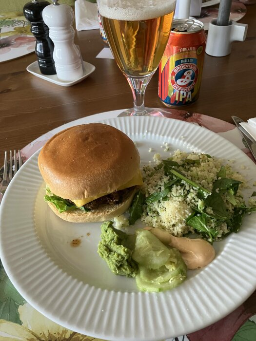 Cheeseburgare, bulgursallad, avokado, öl i glas, IPAdryckesburk, salt- och pepparkvarn på matbord.