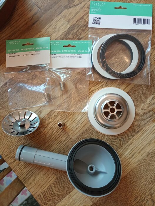 Reservdelar på träbord: packningar, skruvar, ventil, sil och siphon för köksvask. Förpackningar märkta "Contura Steel."