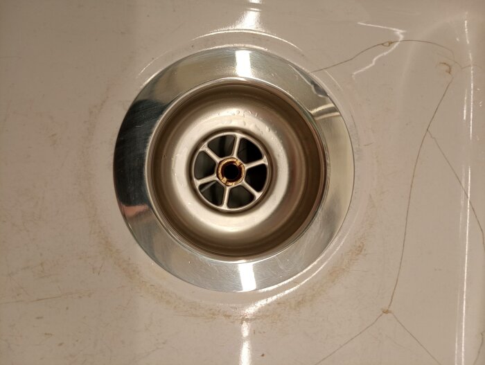 Närbild på en smutsig diskho med synlig avloppsbrunn och repor.