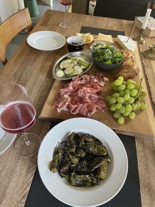Ett välarrangerat bord med charkuterier, ostar, grönsaker, bröd, grillade paprikor och två glas rött vin.