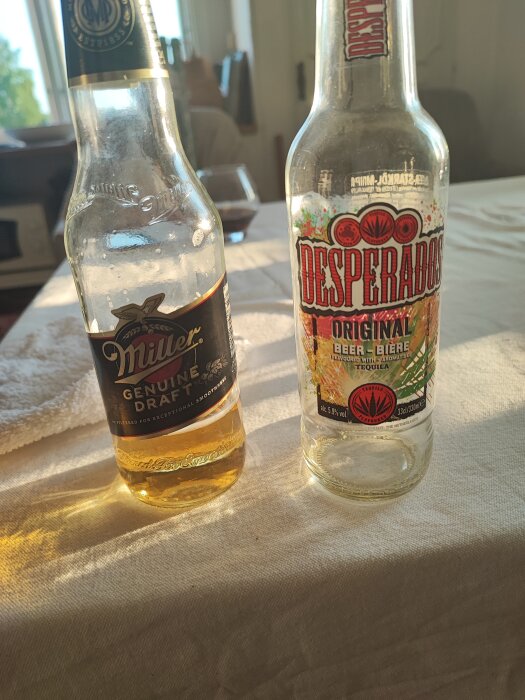 Två ölflaskor på ett bord i solljus, en Miller och en Desperados, delvis vattenfyllda.