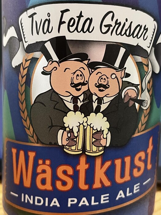 Ölflaska med "Två Feta Grisar" och "Västkust India Pale Ale", tecknade grisar i kostym håller ölglas.