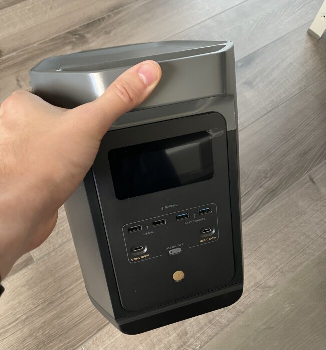 Hand håller en bärbar batteriladdare med USB-portar och en display.