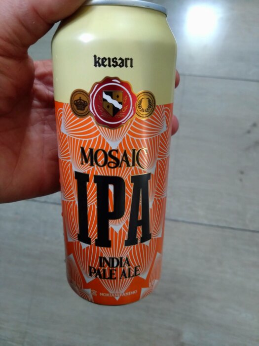 En hand håller en burk Mosaic IPA-öl med grafisk design i orange och vit.