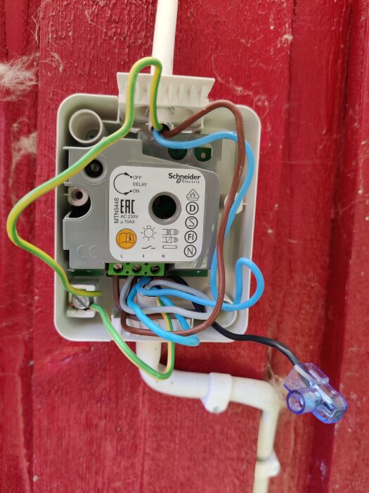 Elrelä från Schneider Electric öppet i installationsdosa, färgglada elektriska anslutningar, röd träbakgrund.
