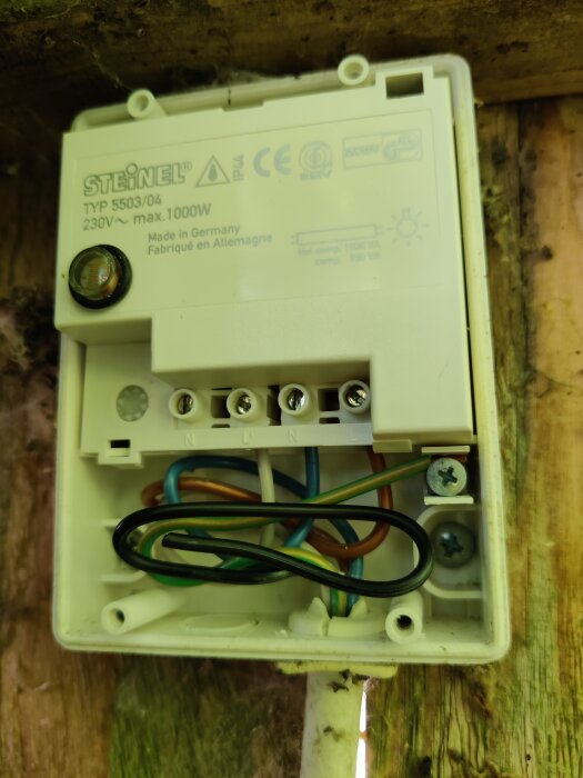 Öppen elektrisk kopplingsdosa med kablar och anslutningar, installerad på en träyta, möjlig fuktskada synlig.