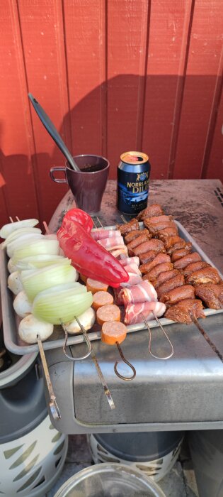 Grillförberedelse med kött, grönsaker, ölburk och kopp utomhus.