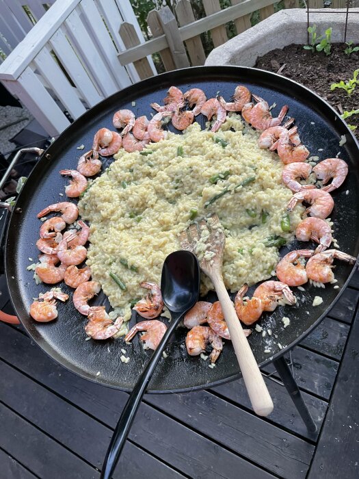 Paella med räkor och sparris på en stor stekpanna utomhus, träredskap, svart slev.