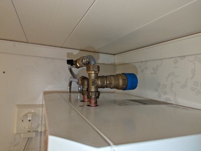 Vattenledningsinstallation under skåp med kopplingar, blå isolering, elektriskt uttag, vit bakgrund, skuggor.