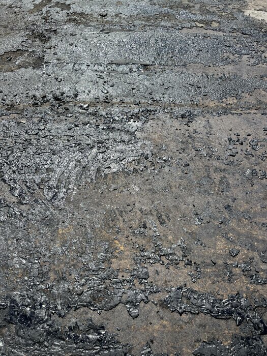 Slitet asfaltunderlag med synlig skadad yta och sprickor, tyder på väderpåverkan eller tung trafik.