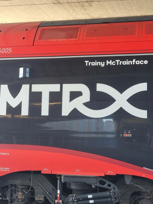 Rödsvart tåg, namn "Trainy McTrainface", målade bokstäver "MTRX", avdelat inomhus.