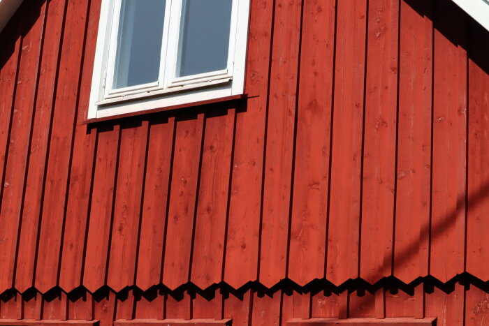 Röd träfasad, fönster, skuggor, svenskt hus, blå himmel, traditionell, arkitektoniska detaljer, dekorativt takutsprång.