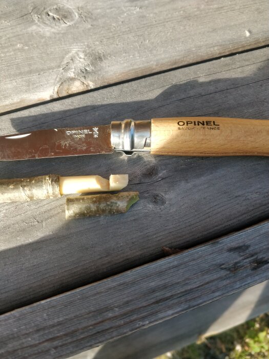 Opinel-fickkniv med delvis bruten handtag på träbänk.