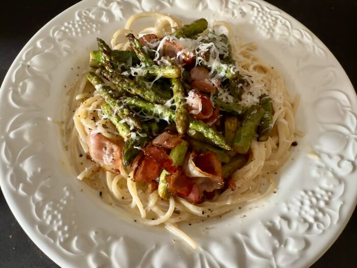 Pasta med sparris, bacon och riven ost på ett detaljerat vitt tallrik.