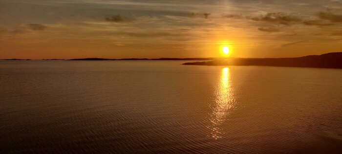 Solnedgång över havet med lugnt vatten och speglande solstrålar. Orangeröd himmel. Ser fredfullt ut.