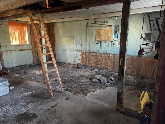 Gammalt utrymme, trästege, verktyg på vägg, orange gardin, smutsigt betonggolv, övergivet intryck.