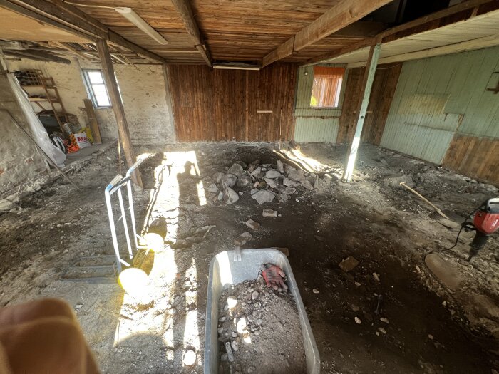 Ett pågående renoveringsprojekt i ett utrymme med borttaget golv, exponerade takbjälkar och byggmaterial synliga.