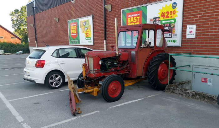 En röd veterantraktor parkerad bredvid en vit modern bil framför en butik med reklamskyltar.