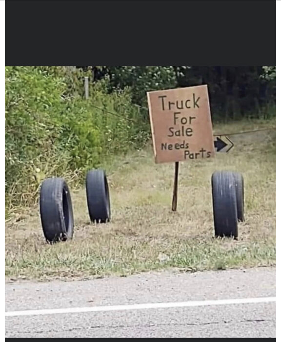 Handskriven skylt, "Truck For Sale Needs Parts", tre däck bredvid, humoristisk, inget fordon synligt, vägkant.