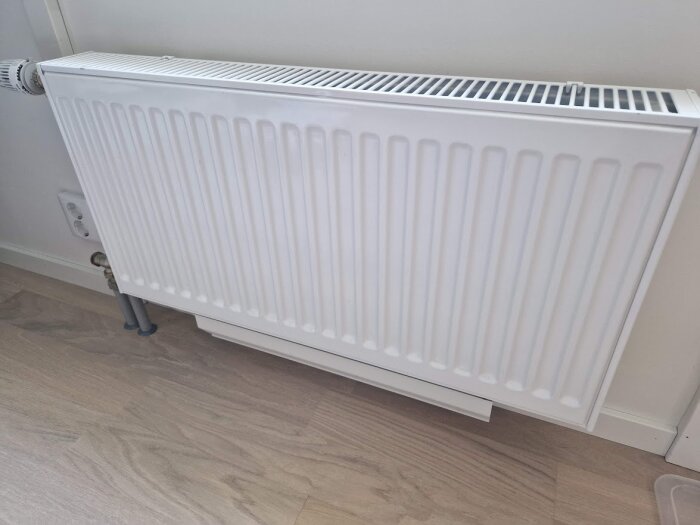 Vit värmeelement/radiator, parkettgolv, minimalism, värmekälla, interiör, vägg, röranslutning, reglerventil, bostadsuppvärmning.