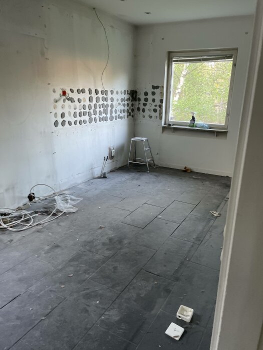 Tomt rum under renovering med spacklade väggar, stege, kabelhögar och skyddad golv.