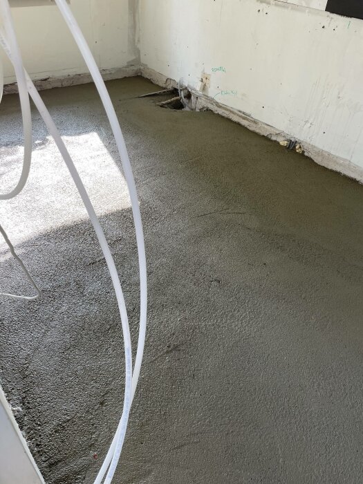 Ett rum under renovering med nylagt, fuktigt avjämningsmassa på golvet och kablarna ligger ovanpå.