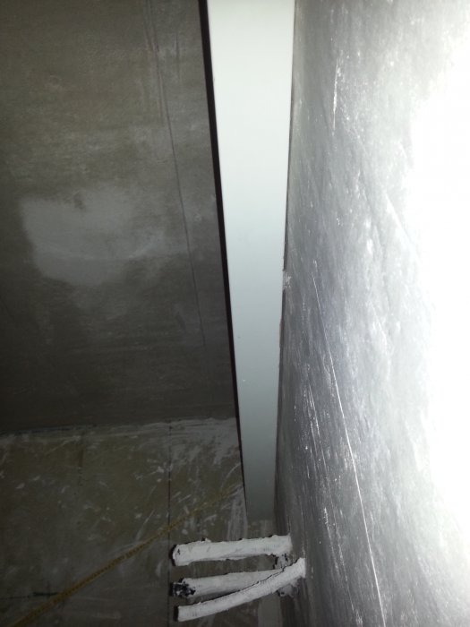 Et vægbillede viser to ujævne overflader adskilt af en planke med udsatte rør nederst, sandsynligvis fra et badeværelses-renoveringsprojekt.