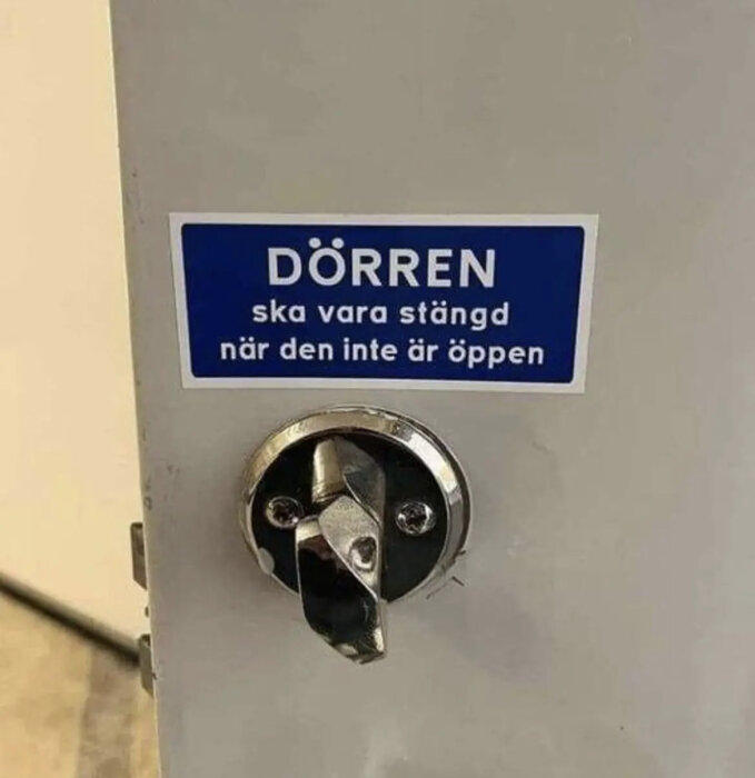 Skylt på dörr säger "Dörren ska vara stängd när den inte är öppen", tillsammans med låshållare. Ironisk, humoristisk.