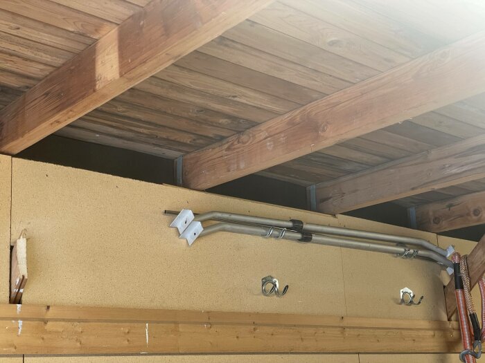 Träbjälklag, kabelrör, krokar på pressad fibervägg, oavslutad installation, inomhus, verktyg på väggen.