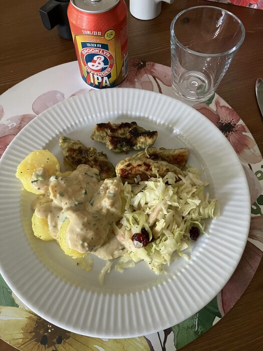 Måltid med potatis, sås, kyckling, sallad, på en blommig tallrik, bredvid en ölburk och tomt glas.