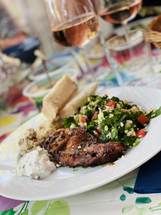 En tallrik med grillat kött, sallad, bröd, tzatziki, rosévin i bakgrunden, somrig måltid, inbjudande middagsatmosfär.