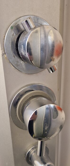 Metallisk dörrhandtag och låscylinder, använda, med speglande ytor, i vertikalt format.