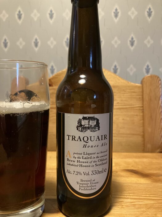 Ölflaska, Traquair House Ale, halvfullt glas, tapetbakgrund, träunderlag, skotsk, alkoholprocent anges.