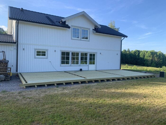 Stort vitt hus med nybyggd ommålad veranda, klar himmel, gräs, träd längre bort.