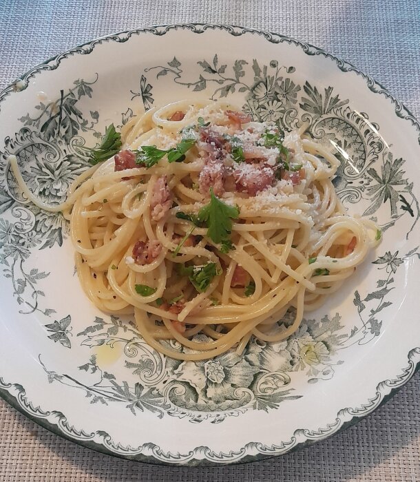 Ett fat spaghetti carbonara med parmesan och persilja på dekorerad tallrik.