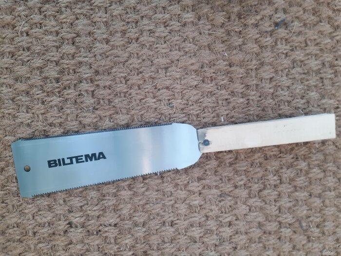En handfogsvans med trähandtag på en brun kokosmatta. Märket "BILTEMA" syns tydligt på bladet.
