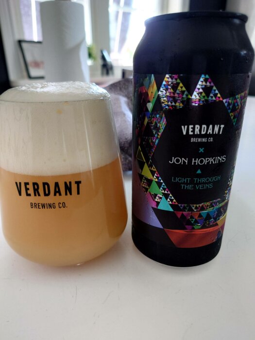 Ett glas öl med tjockt skum bredvid en ölburk från Verdant Brewing Co.