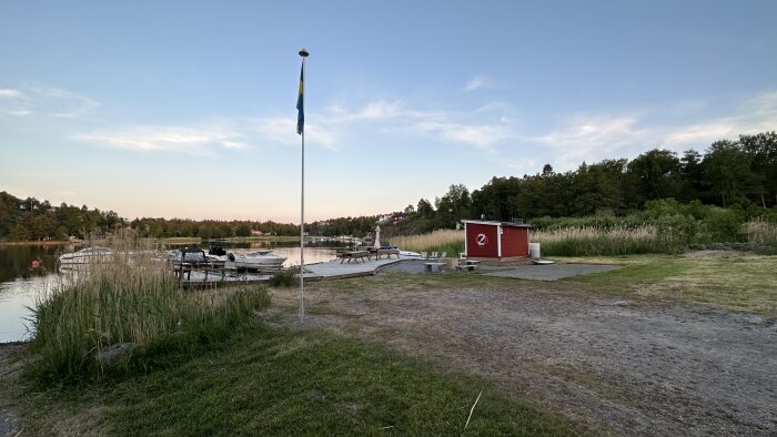 En svensk småbåtshamn vid sjön vid skymning, med bryggor, båtar och en svensk flagga.