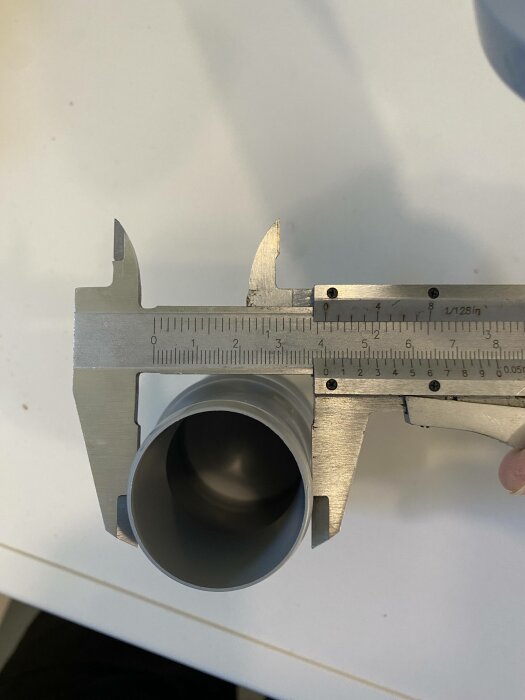 Skjutmått mäter diameter på cylindriskt objekt mot vit bakgrund. Metall, precision, verktyg, teknik, mätinstrument.