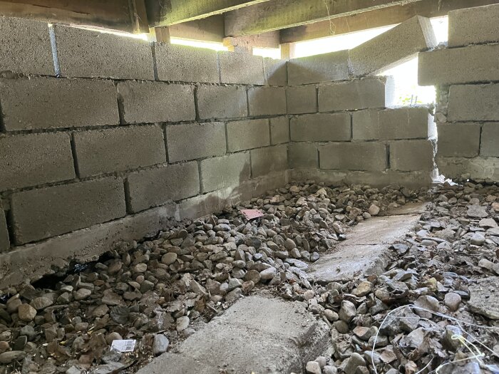Under en byggnad med betongblock och stenar, träbjälkar, delvis dagsljus. Nedskräpat, övergivet utrymme.