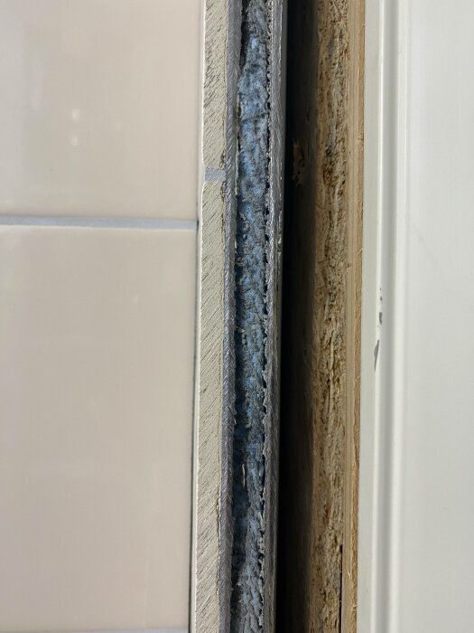 Närbild på en dörrkarm och vägg med synlig isolering och konstruktionsdetaljer. Färger: beige, vit, grå.