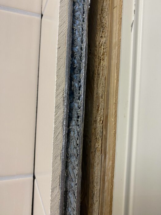 Tätningsskum mellan vägg och dörrkarm, ojämnt applicerat, expanderat, synliga trästrukturer, byggmaterial, renoveringsdetalj.