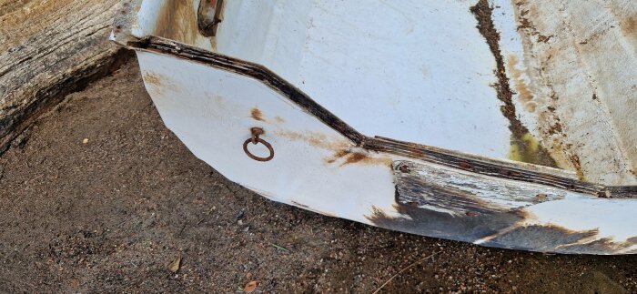 En rostig ring på en slitna båtens skrov vid trä och sand. Färgflagnande, förfall, närbild, skadad, övergiven.
