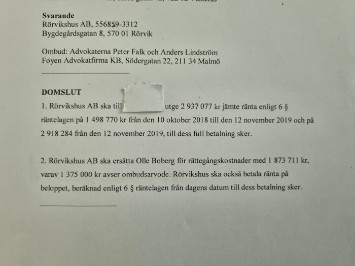 Fotografi av domslut med text, ekonomiska belopp, juridisk information, och en otydlig plats där text täcks.