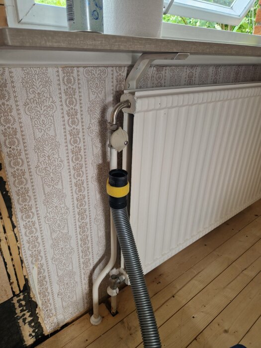 Element med rörsystem, kopplad till flexibel slang, vid tapetserad vägg, vid fönster och trägolv.