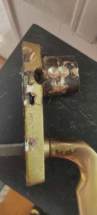 Guldfärgad dörrkarm och handtag, skadad säkerhetskedja, svart marmorbakgrund, behov av reparation.