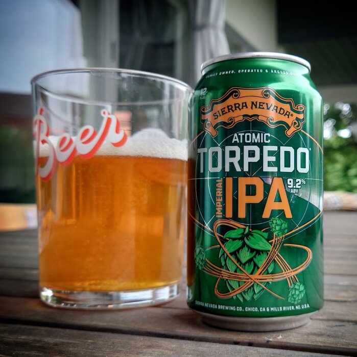 Ett glas öl bredvid en "Atomic Torpedo IPA" burk från Sierra Nevada på ett bord.