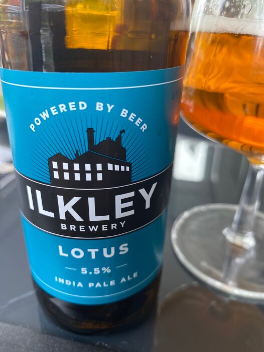 En ölflaska från Ilkley Brewery med namnet Lotus IPA, bredvid ett delvis fyllt ölglas.