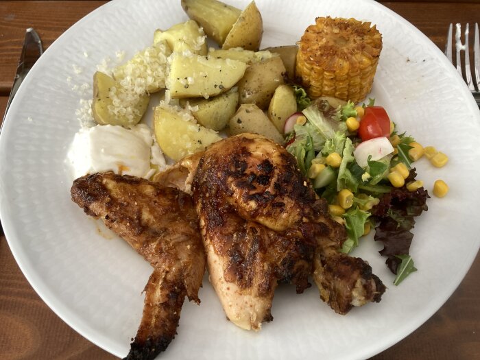 Ett fat med grillad kyckling, potatisar, majs, sallad och vitlökssås. Färgrikt och aptitretande måltid.