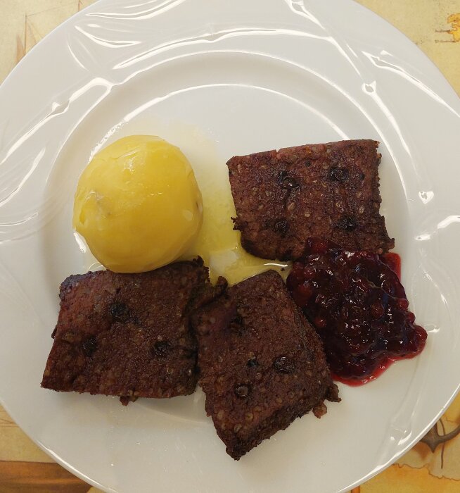 Tre bitar kladdkaka, en kula vaniljglass och lingonsylt på en vit tallrik.